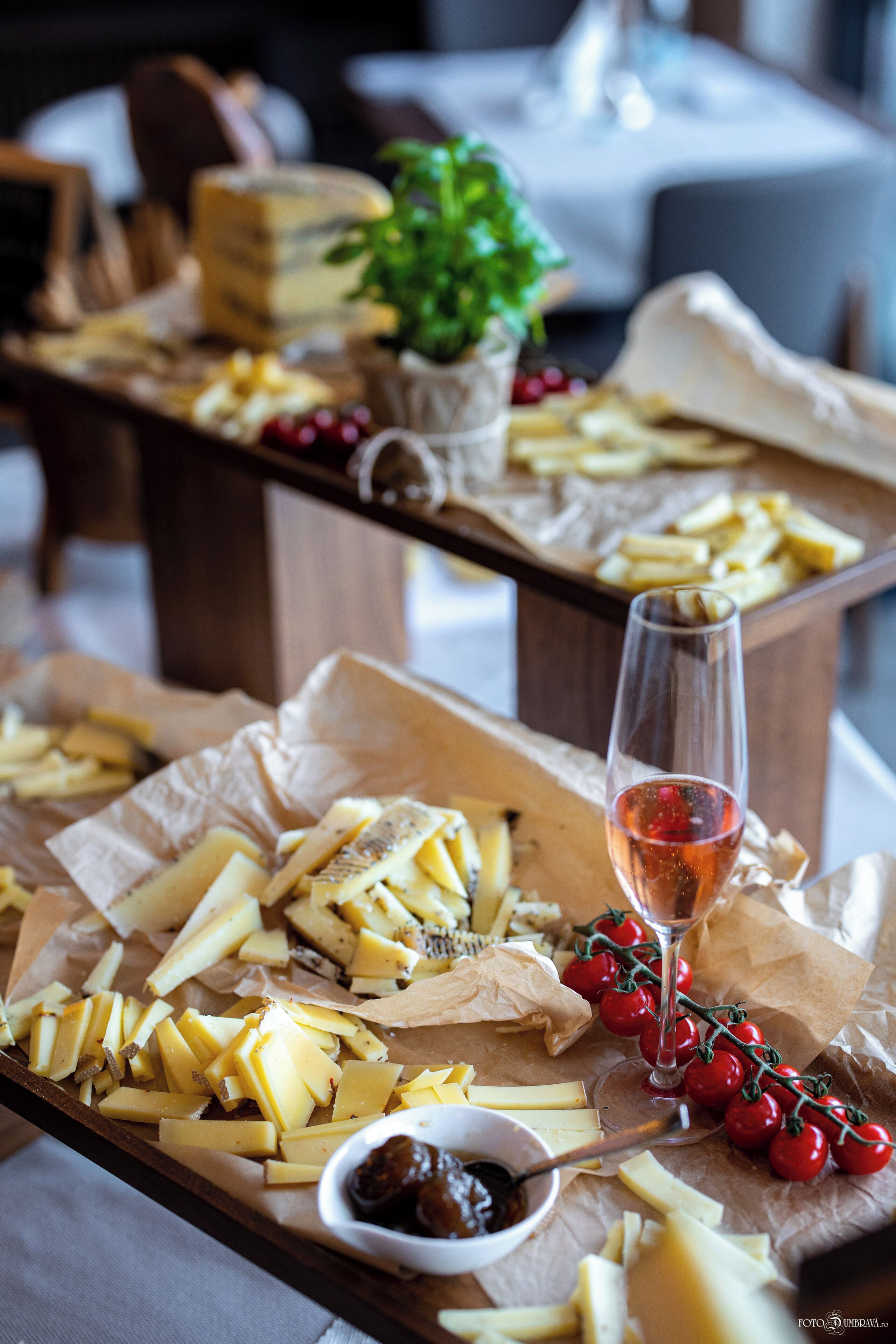 A cheese board with various cheeses, a glass of wine, and cherry tomatoes on a wooden table.