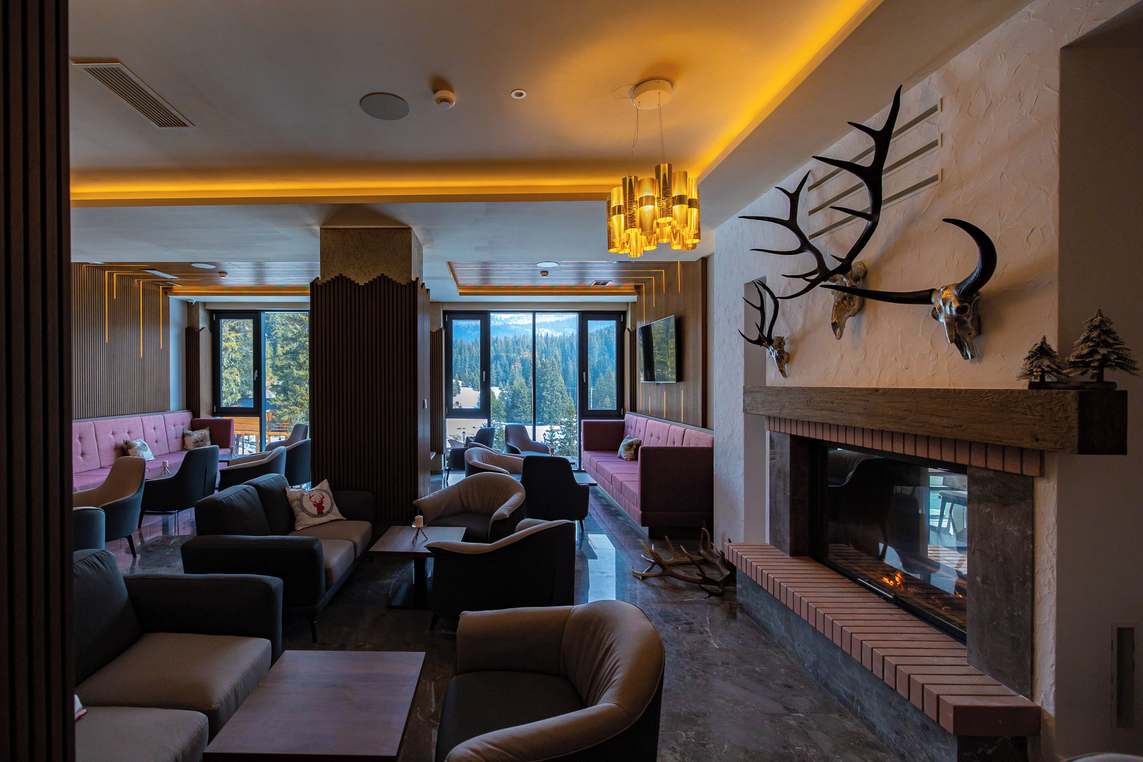 A modern lounge with leather sofas, a fireplace, and a large window overlooking a forest.