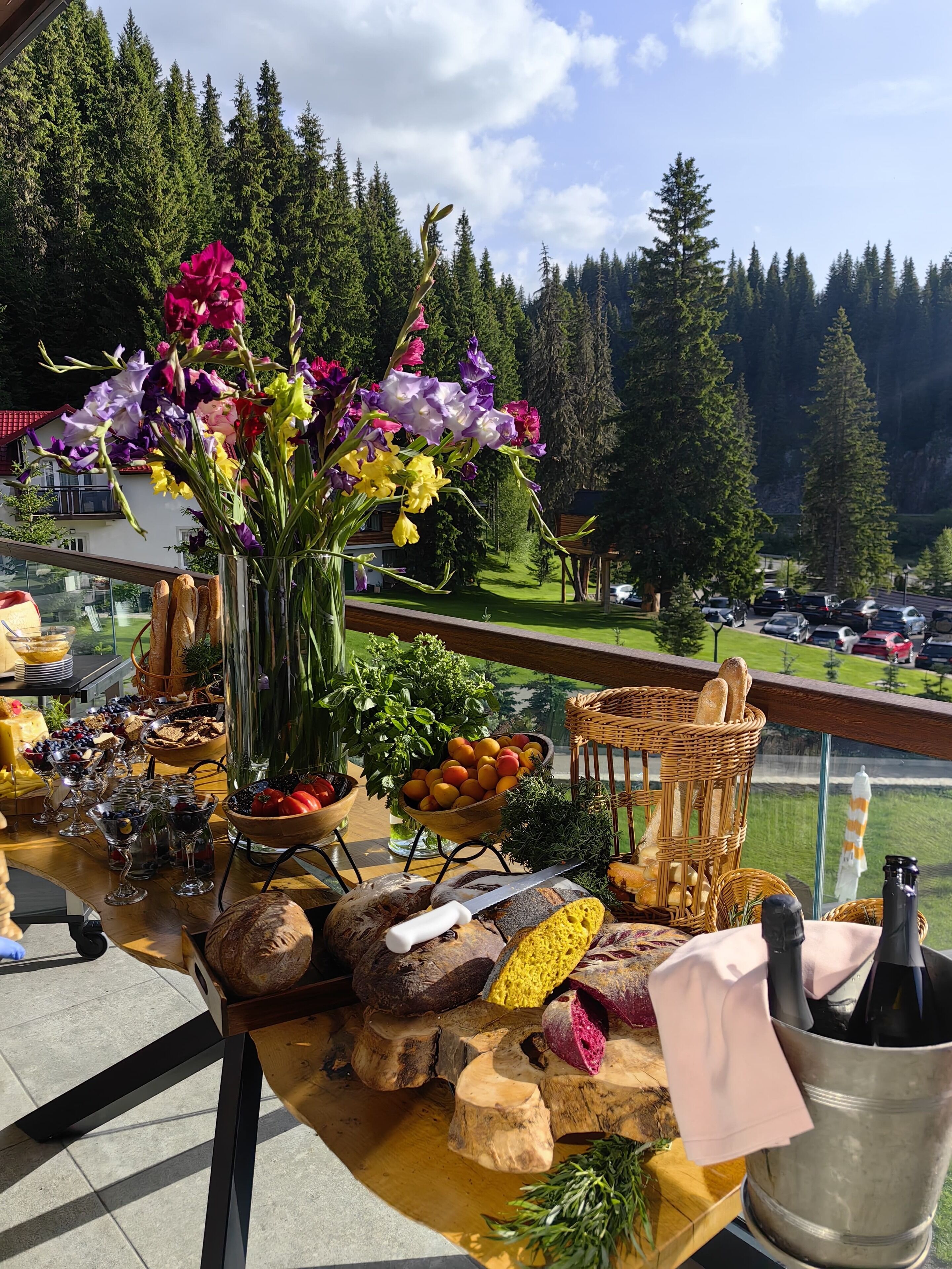 A buffet table with various food items and a vase of flowers, overlooking a forested area.