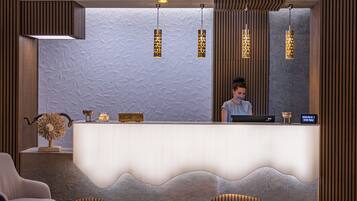 A reception area with a modern design, featuring a textured wall, a reception desk with a wave-like front, and pendant lighting.