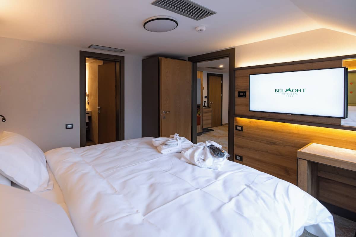 A hotel room with a large bed, a television mounted on the wall, and a wooden headboard.