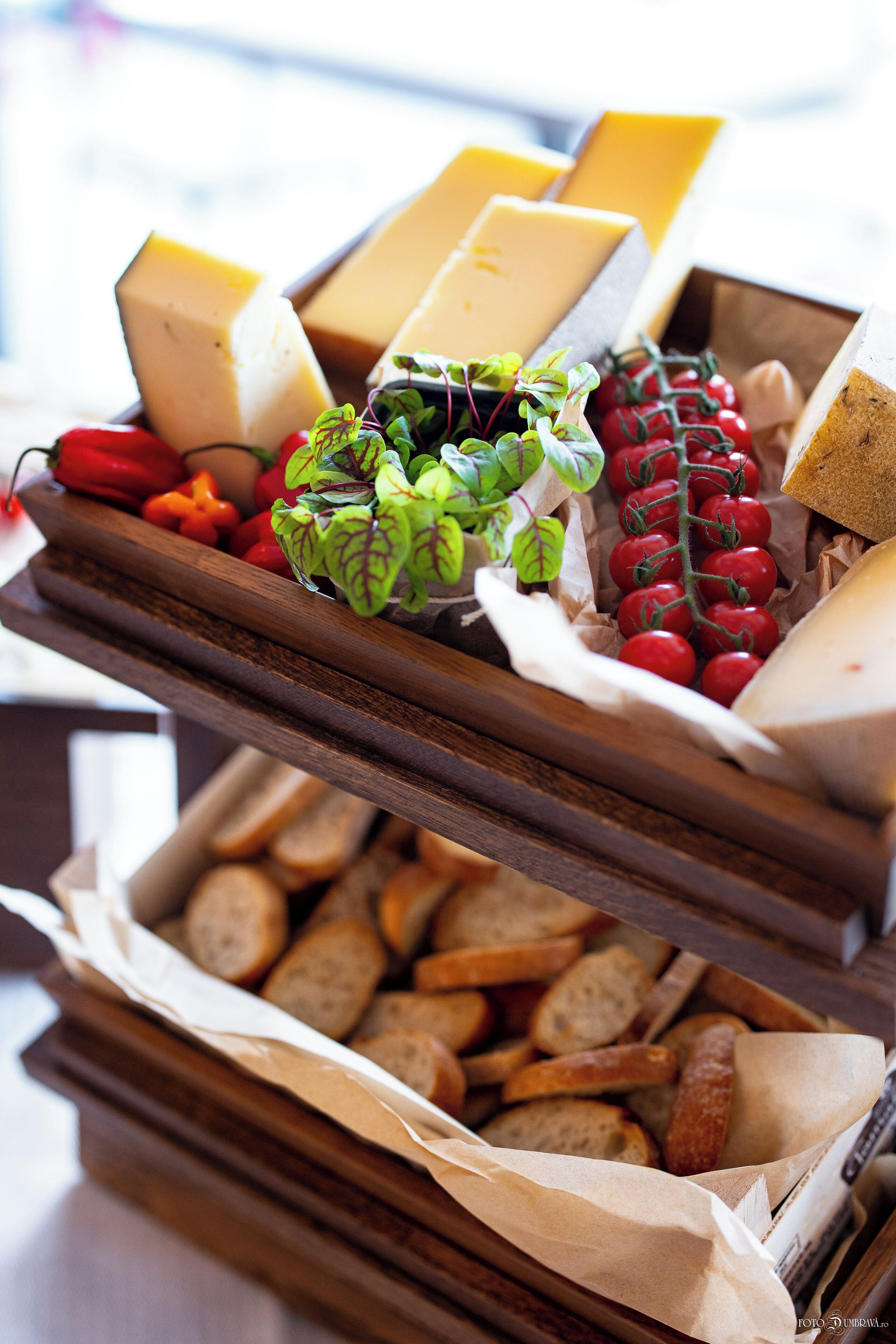 A wooden board with various cheeses, tomatoes, and bread slices.