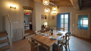Comedor con mesa de madera dispuesta para cuatro personas, rodeada de sillas, bajo vigas de madera a la vista.