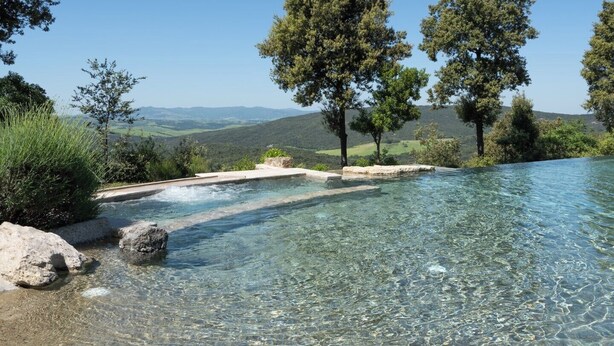 Una piscina cristalina con vistas a colinas y árboles a lo lejos.