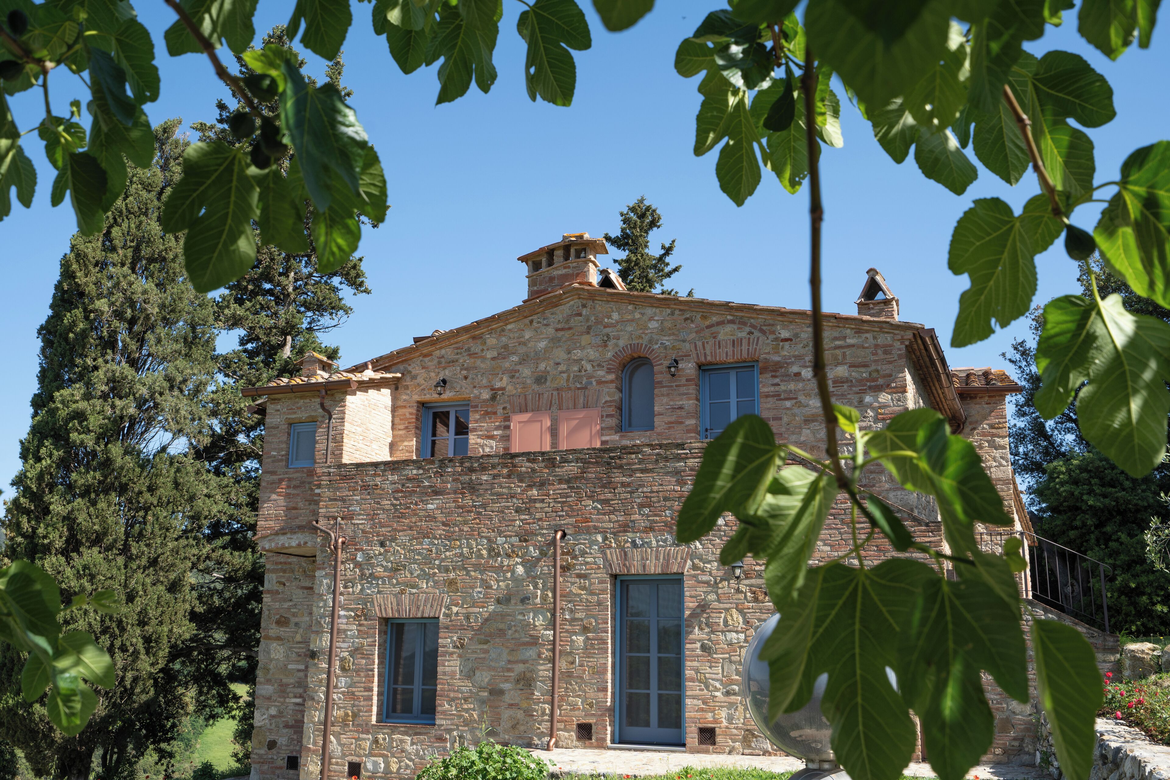 A stone building with multiple windows and a chimney, surrounded by trees.