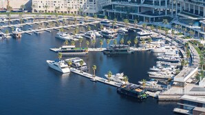 Un port de plaisance doté de plusieurs quais et abritant de nombreux bateaux, entouré de bâtiments modernes et de palmiers.