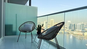 Un balcon avec deux fauteuils en osier, une plante en pot et une vue sur la ville.