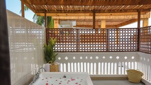 Un baño con bañera, paredes de azulejos blancos, techo de madera y valla blanca.