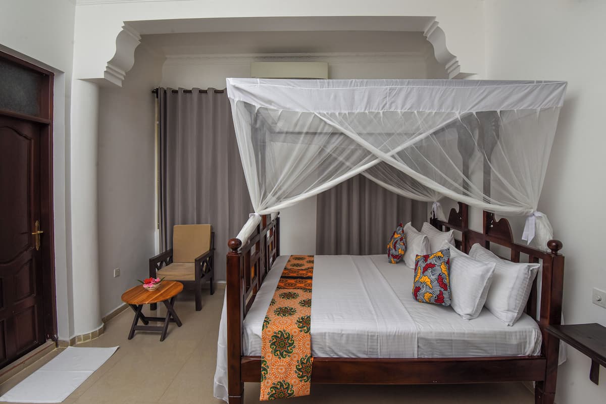 Un dormitorio ordenado con cama de madera, ropa de cama blanca, dosel y una pequeña mesa con una silla.
