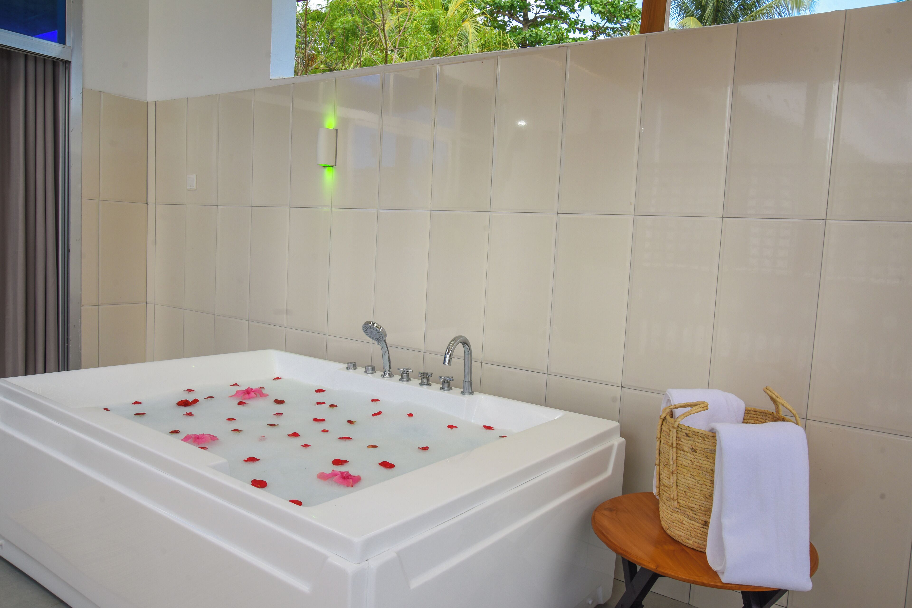 Une salle de bain moderne avec une grande baignoire remplie de pétales de roses, une chaise en bois avec une serviette et un panier en osier.