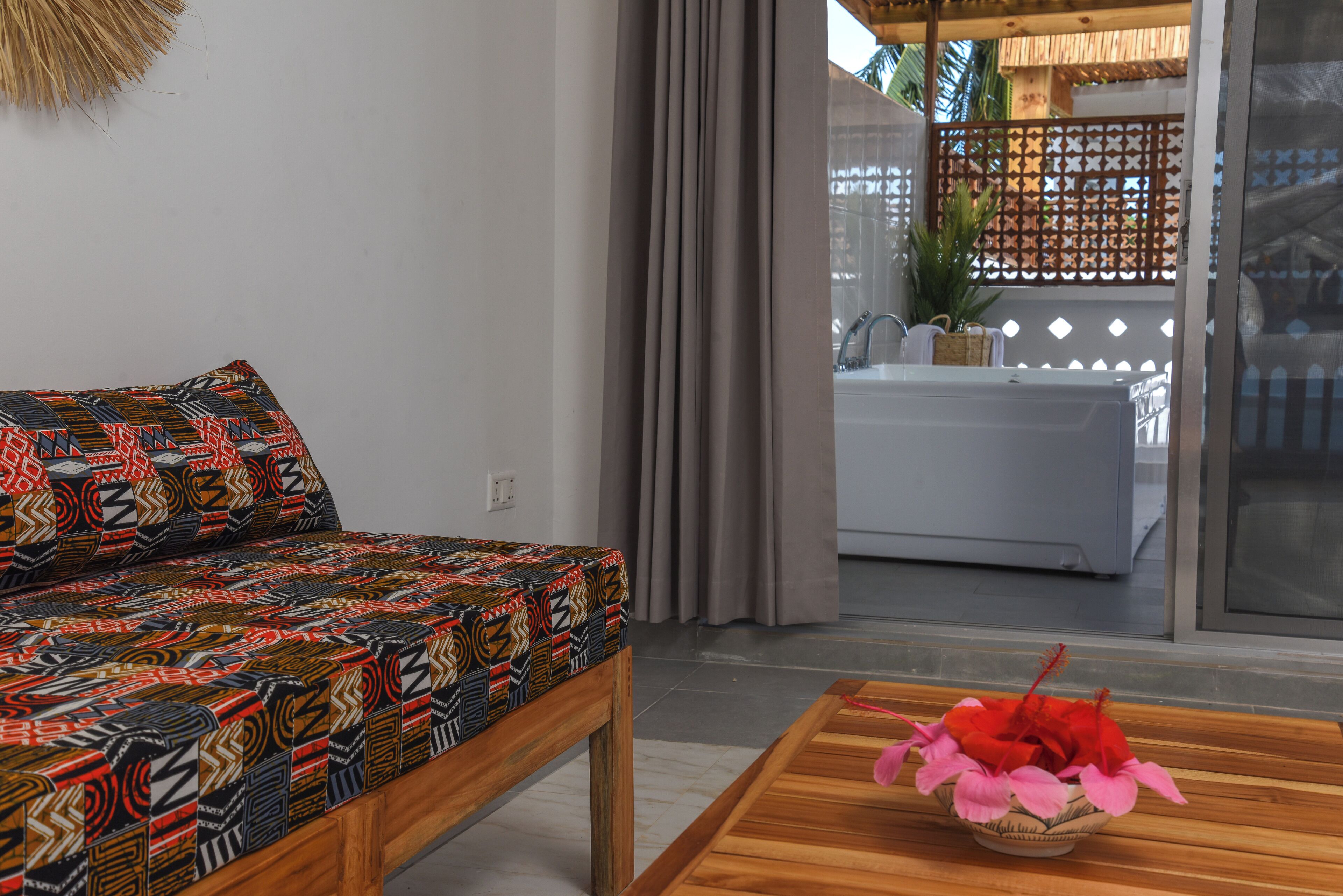 Een kamer met een gestreept bankstel, een houten salontafel met een bloevas, en uitzicht op een badkamer door een schuifdeur.