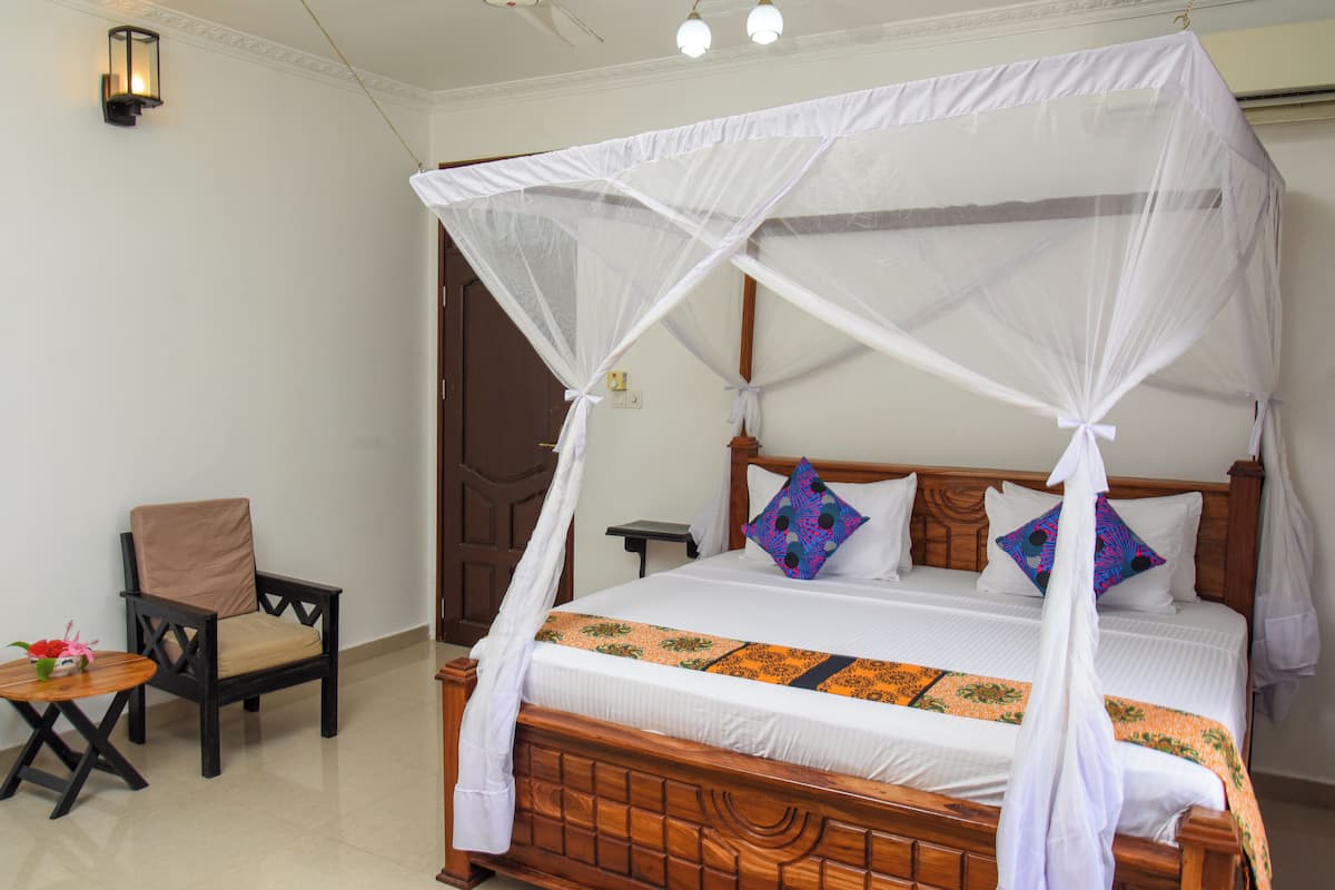 Un dormitorio con una cama con dosel, una silla de madera, una mesita pequeña y una mesita de noche.
