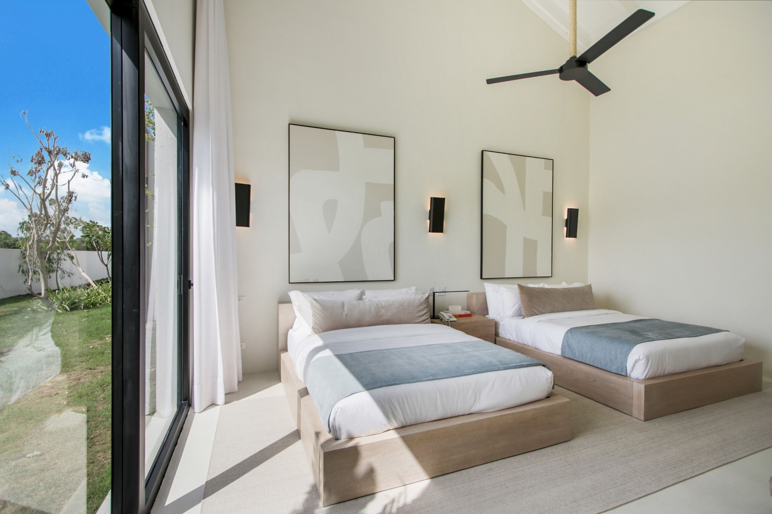 Ein modernes Schlafzimmer mit zwei Betten, großen Fenstern und einem Deckenventilator.