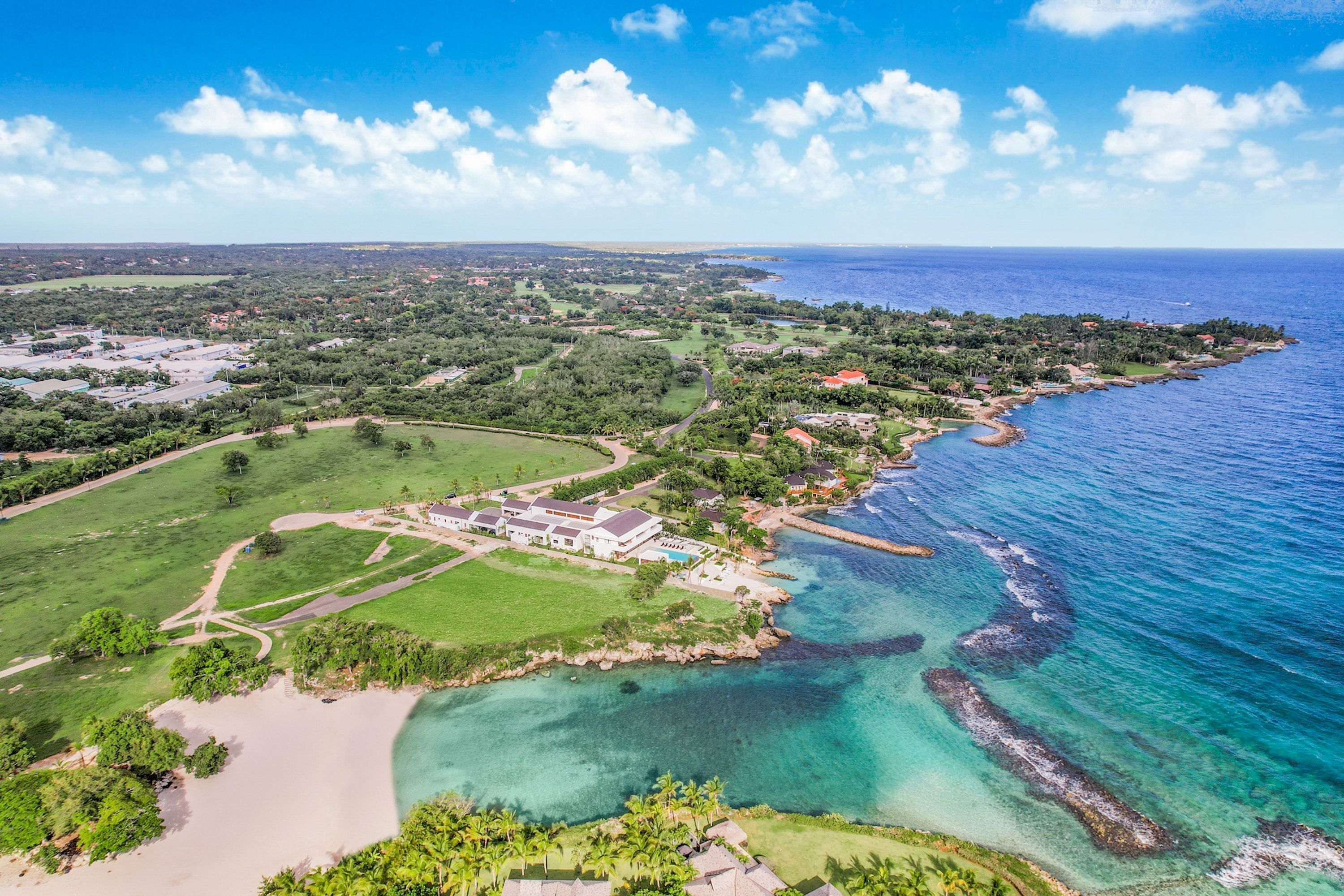 Vista aérea de un complejo turístico costero con un edificio grande, una playa y aguas azules cristalinas.