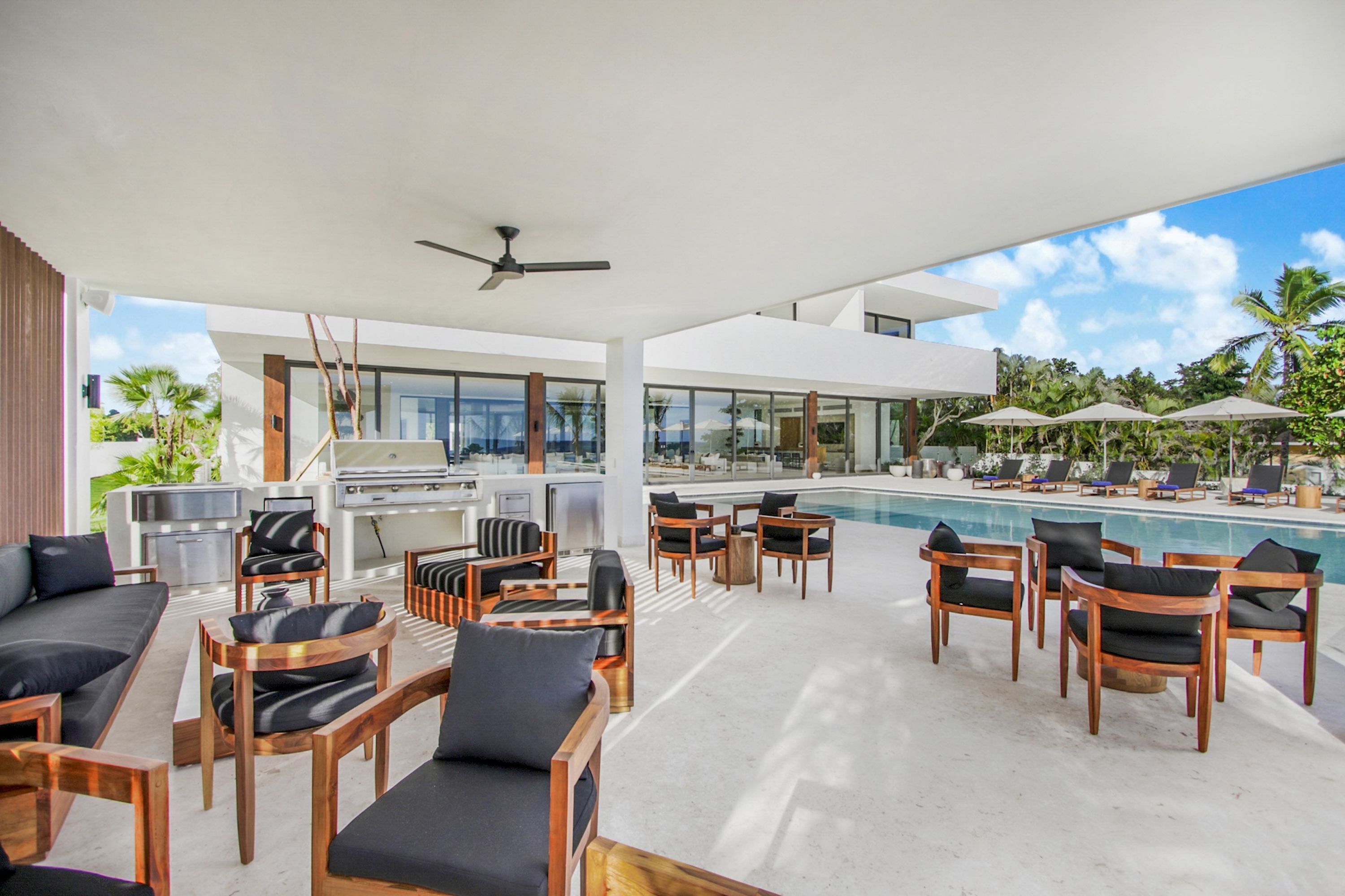 Un espace de détente extérieur moderne, doté d’une piscine, de mobilier en bois et offrant une vue sur un paysage tropical.