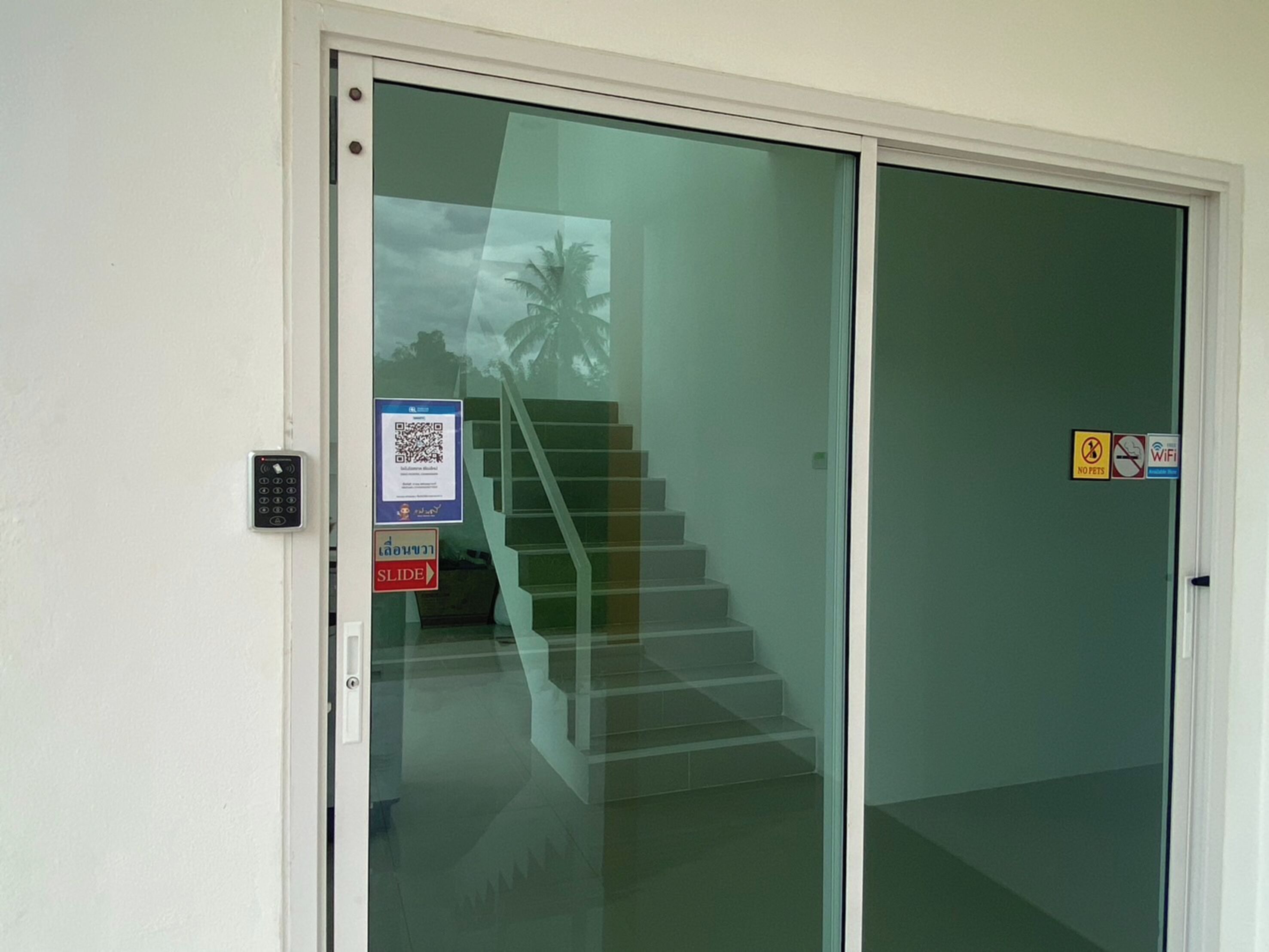 A glass door with a sliding mechanism, a QR code, a 'No Pets' sign, and a 'No Smoking' sign.