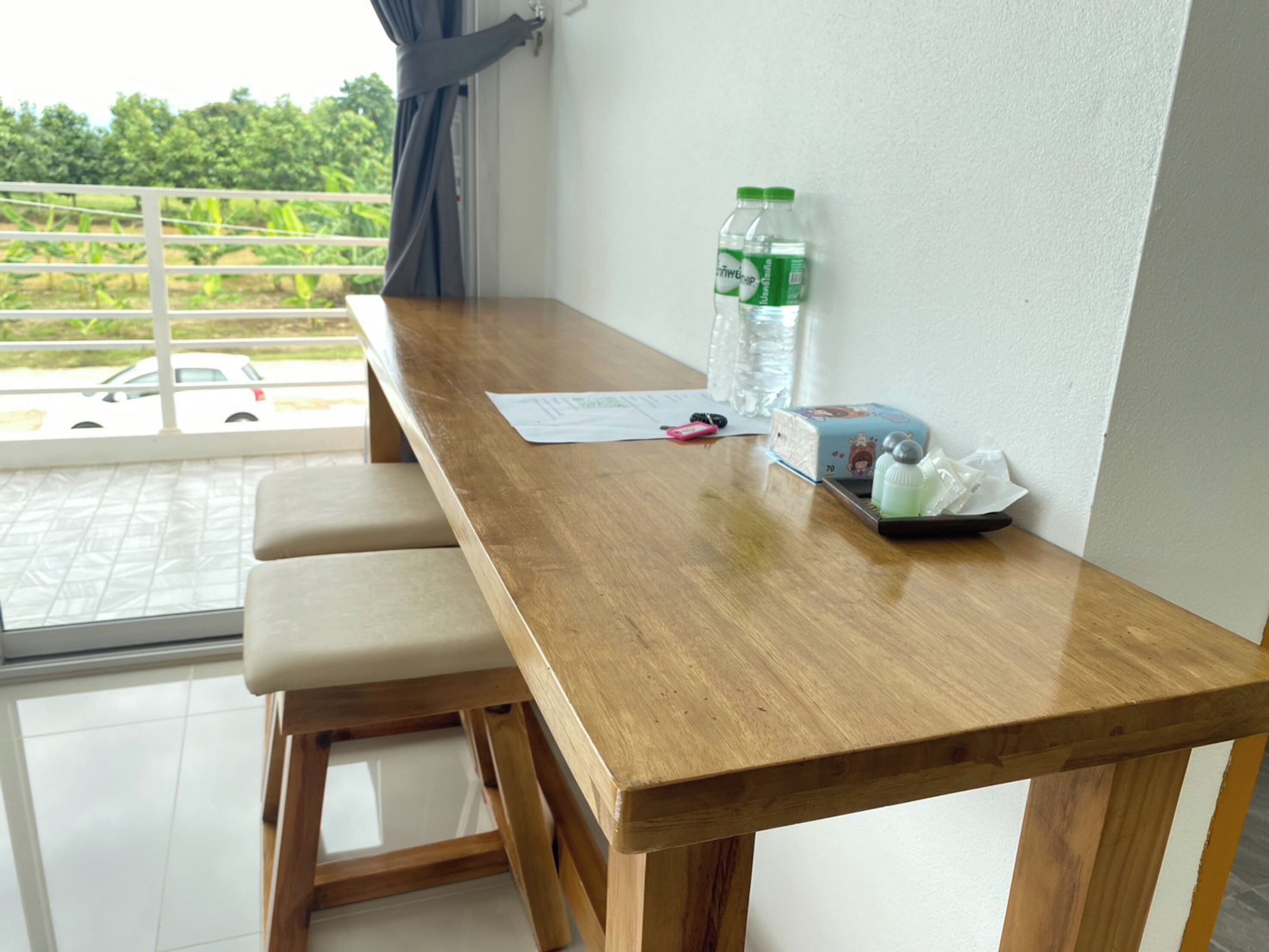A wooden table with a pair of cushioned stools, a water bottle, a tissue box, and a small tray with tissues.