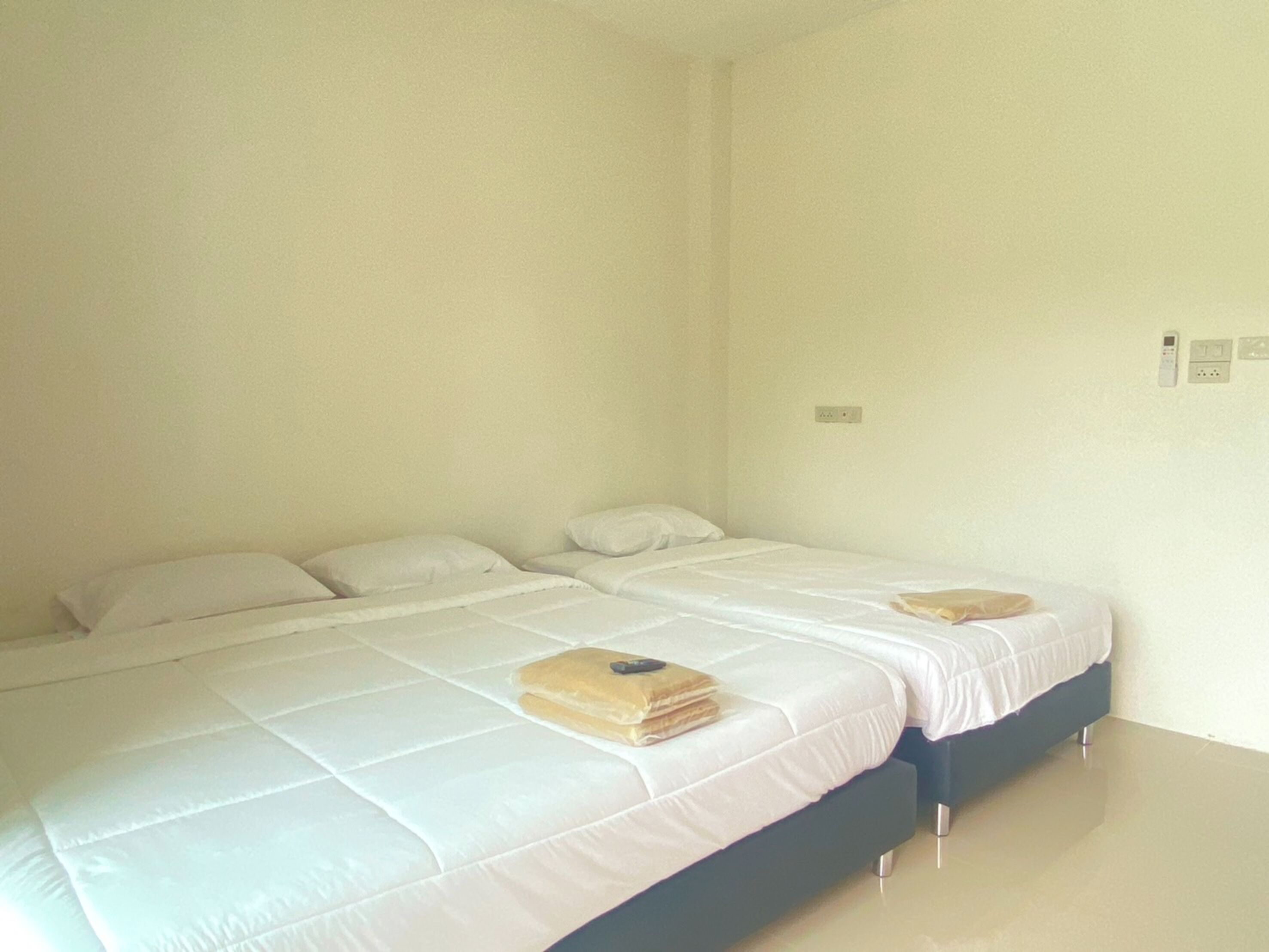 A clean, minimalist bedroom with two single beds, a flat floor, and a plain wall.
