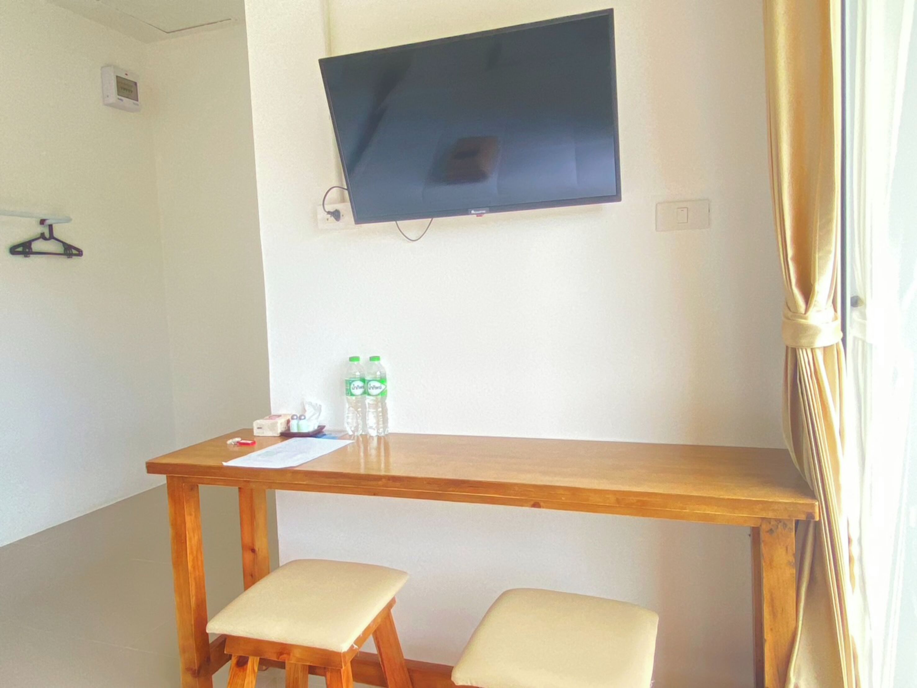 A hotel room with a wooden desk, two chairs, a flat-screen TV mounted on the wall, and two bottles of water on the desk.