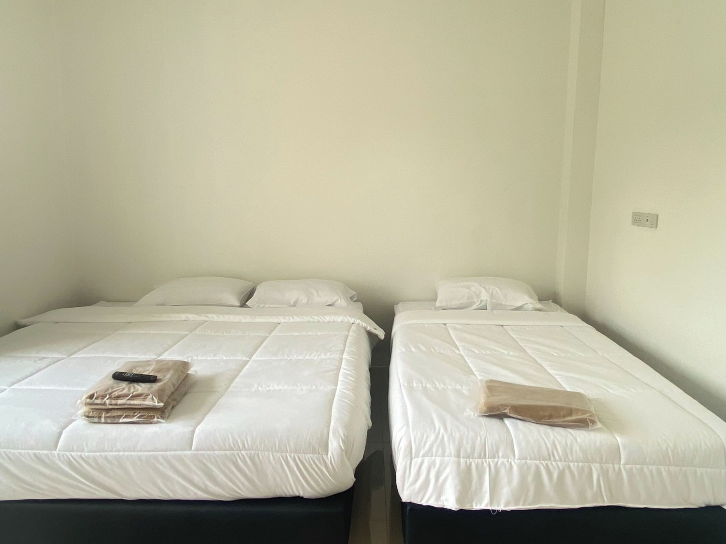 Dos camas individuales con ropa blanca de cama y almohadas, un control remoto y una toalla doblada en cada cama.