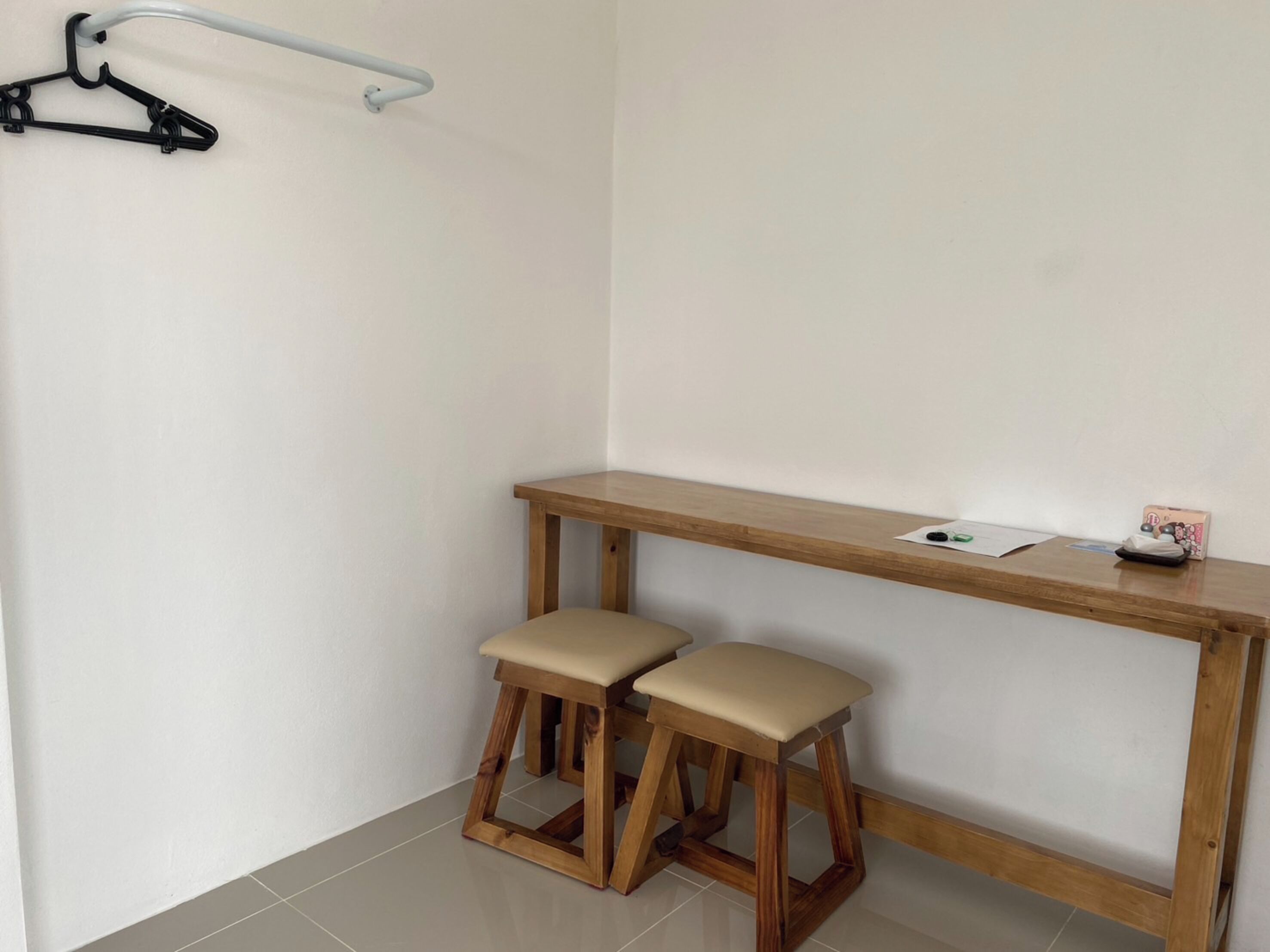 A small, clean room with a wooden desk, two matching stools, a coat rack, and a small table with a few items on it.