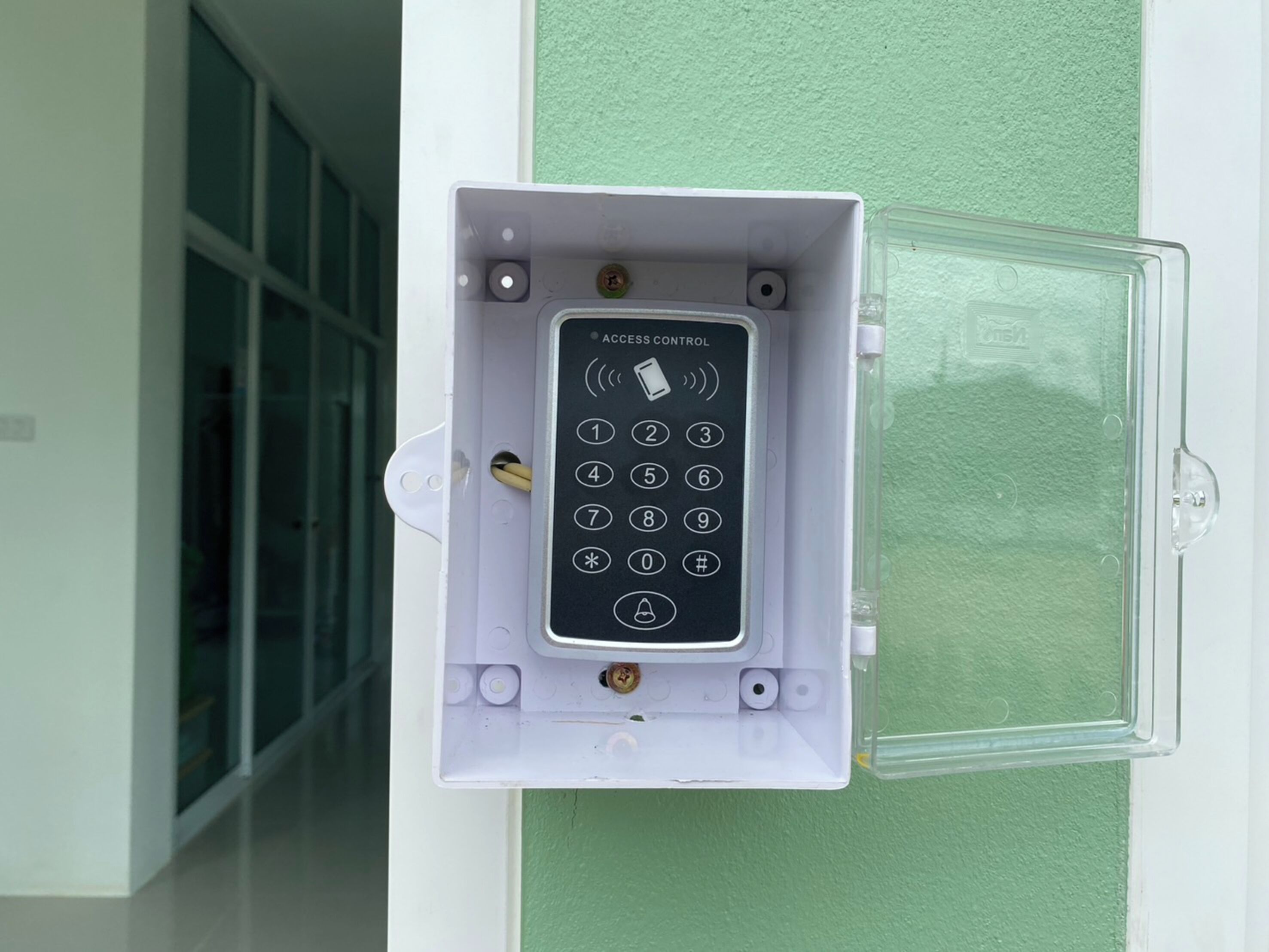 A keypad access control panel mounted on a wall, with a clear glass door beside it.