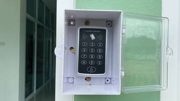 A keypad access control panel mounted on a wall, with a clear glass door beside it.