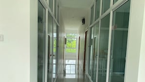 A long, narrow hallway with glass doors on both sides, leading to a bright room with a view of greenery outside. - Dino Homestay (Mae Taeng)