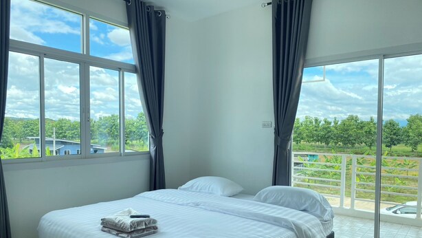 A bedroom with a bed, two windows, and a view of greenery and a pool. - Dino Homestay (Mae Taeng)