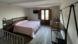 Een slaapkamer met een bed, een bureau, een stoel, een televisie en een raam met open luiken.