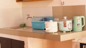 Eine Küche mit Spüle, einem blauen Aufbewahrungsbehälter, einem weißen Slow-Cooker und einem grünen Wasserkocher.