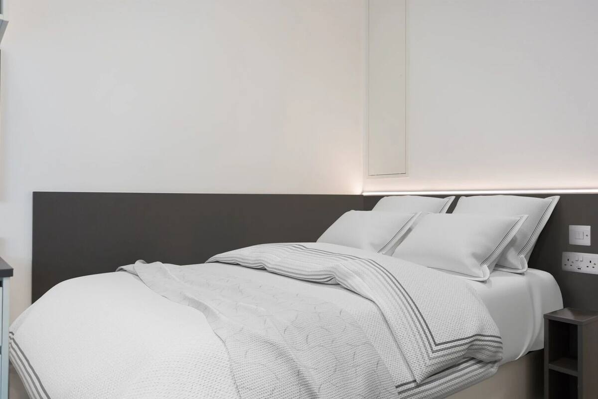 A modern bedroom with a bed, nightstands, and a wall-mounted light fixture.