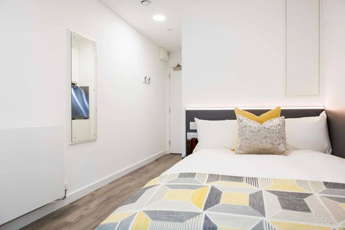 A hotel room with a large bed, a bedside table, a mirror, and a wall-mounted air conditioning unit.