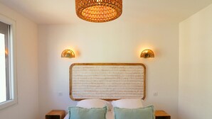 Une chambre à coucher avec un grand lit, deux tables de chevet, une tête de lit en osier et un luminaire suspendu.