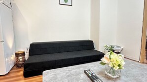 A modern living room with a black sofa, a small table with a remote control, and a vase with flowers. - SOLASIA residence Kitaueno501 (Tokyo)