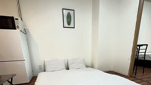 A neatly made bed with a folded towel, a small table, and a chair in a simple room with white walls and wooden flooring. - SOLASIA residence Kitaueno501 (Tokyo)