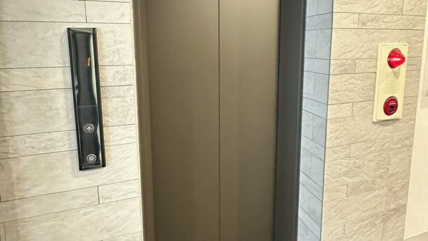 A modern elevator with a control panel on the wall, a red emergency button, and a tiled floor. - SOLASIA residence Kitaueno501 (Tokyo)