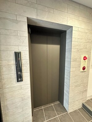 A modern elevator with a control panel on the wall, a red emergency button, and a tiled floor. - SOLASIA residence Kitaueno501 (Tokyo)