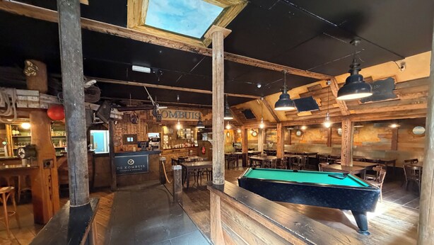 Una mesa de billar, una barra de madera y un área de descanso en un local de estilo rústico.