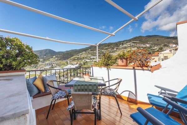 A terrace with a table and chairs, a view of the countryside, and a mountain in the background. - Traditional Ligurian House by Wonderful Italy (Sanremo)