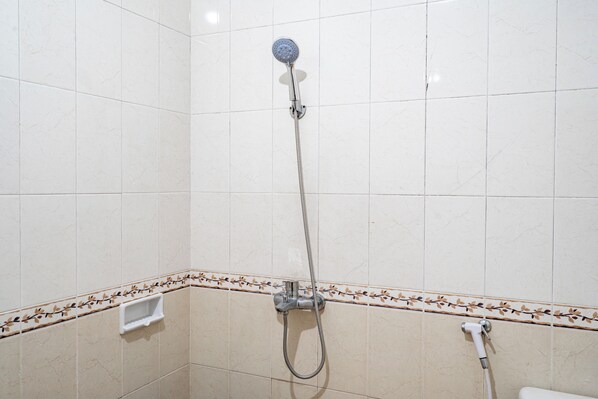 Une salle de bain avec des murs recouverts de carreaux blancs, une pomme de douche et des toilettes.