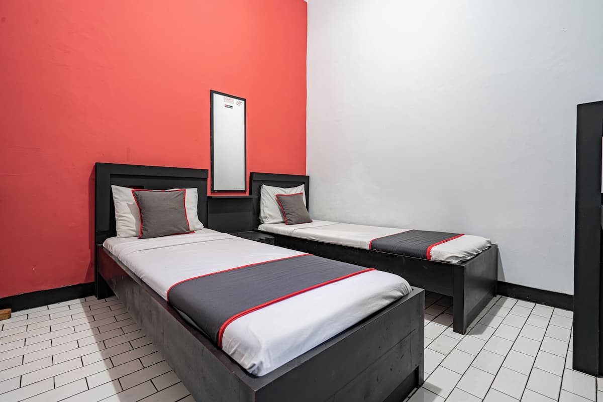 Una camera d'albergo con due letti, una parete rossa e una bianca.