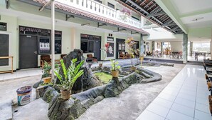 Un vaste espace intérieur doté d’un sol carrelé, de plusieurs coins salon et d’un élément décoratif central en roche, agrémenté de plantes en pot.