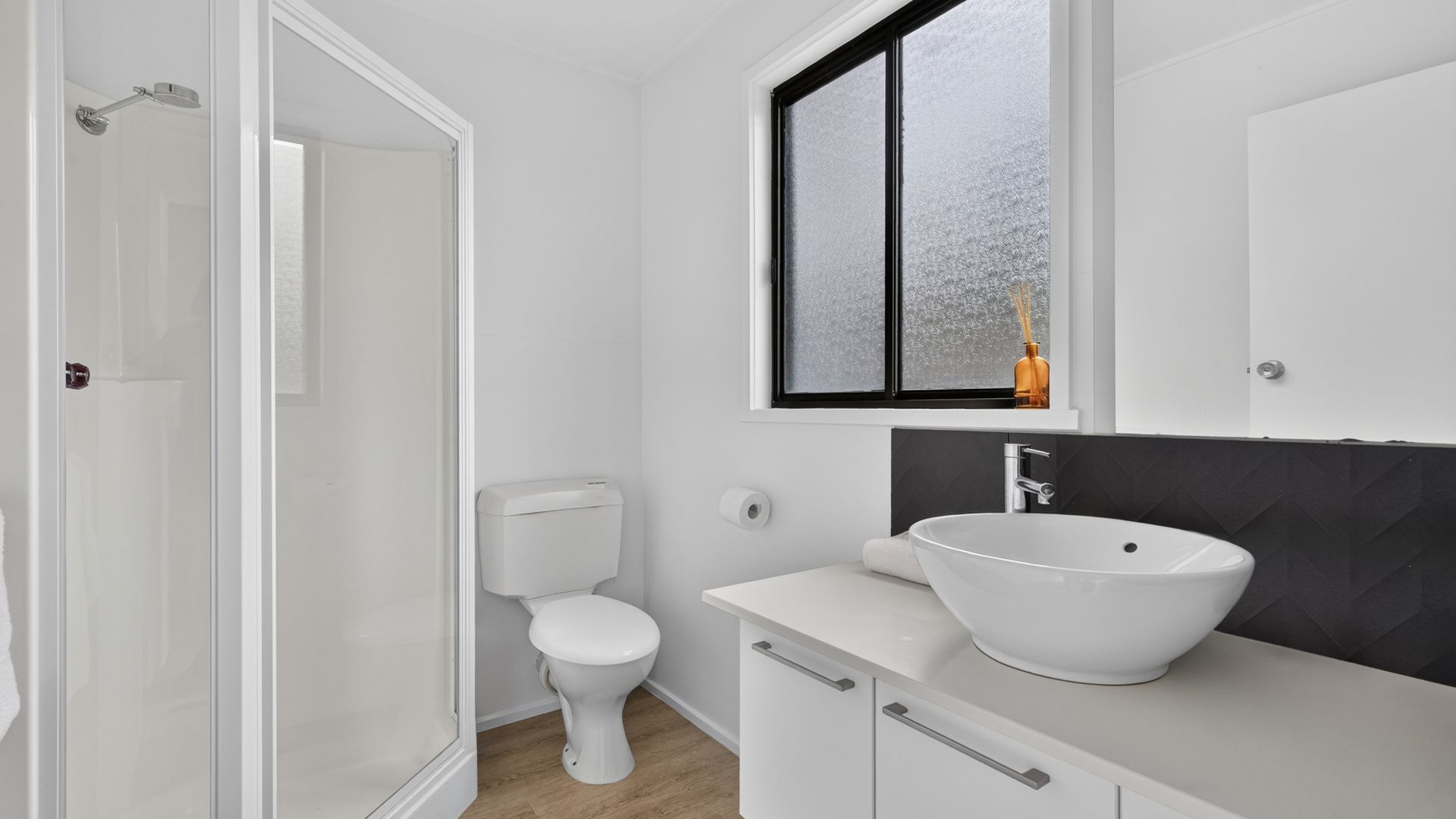 A bathroom with a white toilet, a white sink, and a window with frosted glass.