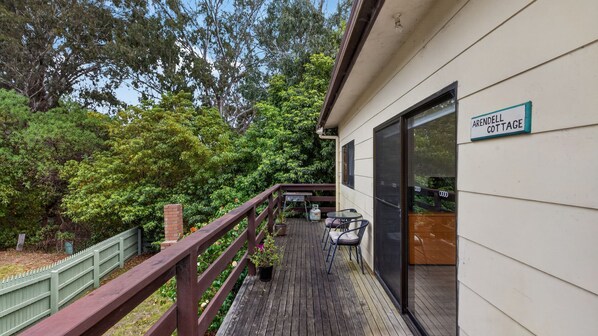 A wooden deck with a glass door leading to a room, surrounded by lush greenery and a sign indicating 'ARRENDELLE COTTAGE'.