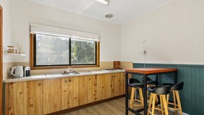Une cuisine avec des meubles de rangement en bois, une fenêtre, un évier, une cuisinière et deux tabourets de bar.