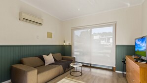 Un salon comprenant un canapé, une petite table, un téléviseur et une porte-fenêtre coulissante donnant sur un balcon.