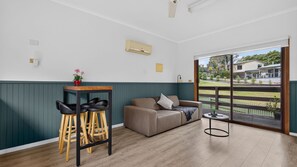 A room with a wooden floor, a sofa, two chairs, a small table, and a window with a view of houses.
