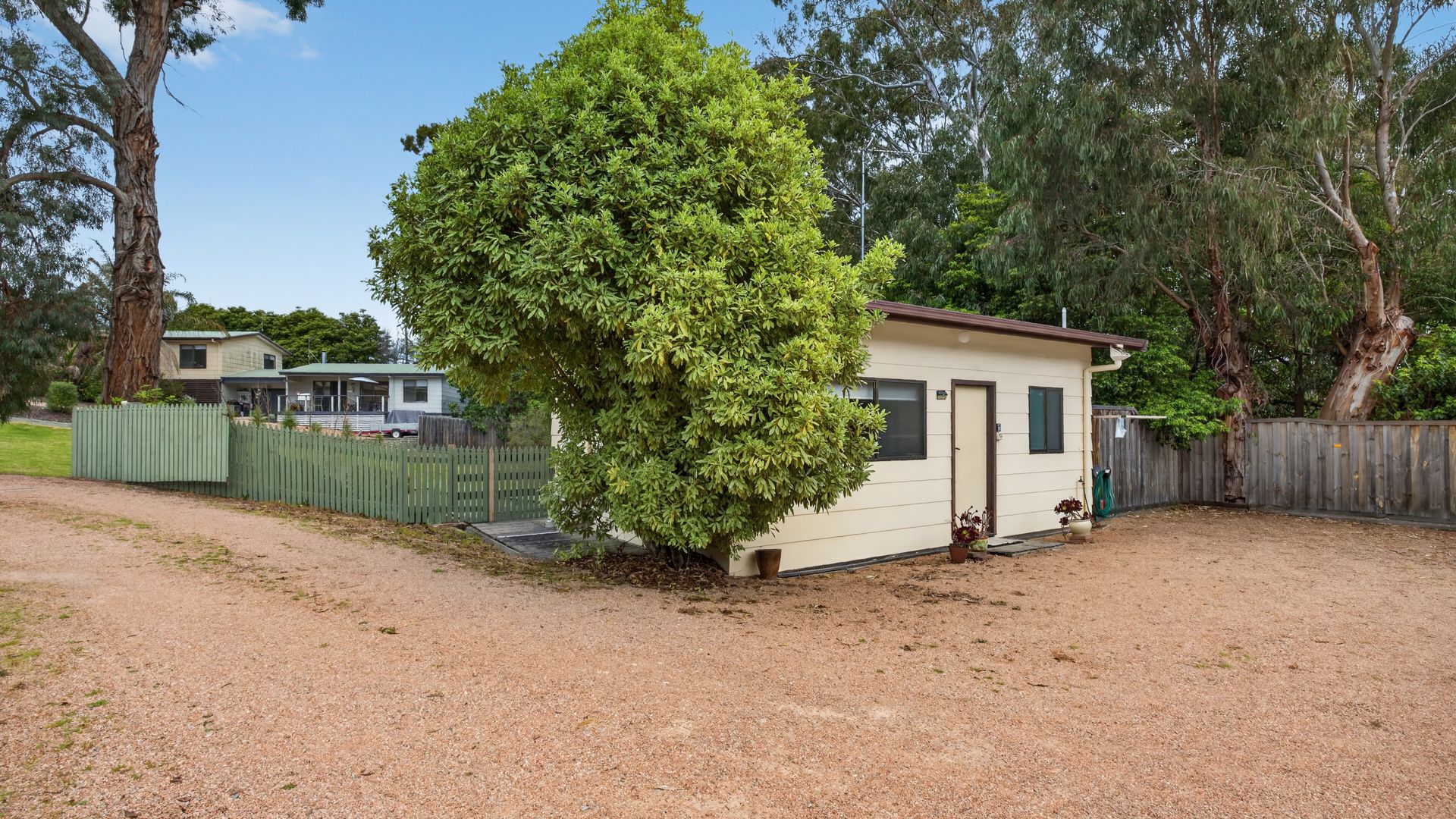 A small, single-story building with a dirt driveway and a fenced yard.