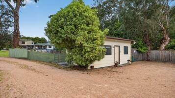 A small, single-story building with a dirt driveway and a fenced yard.